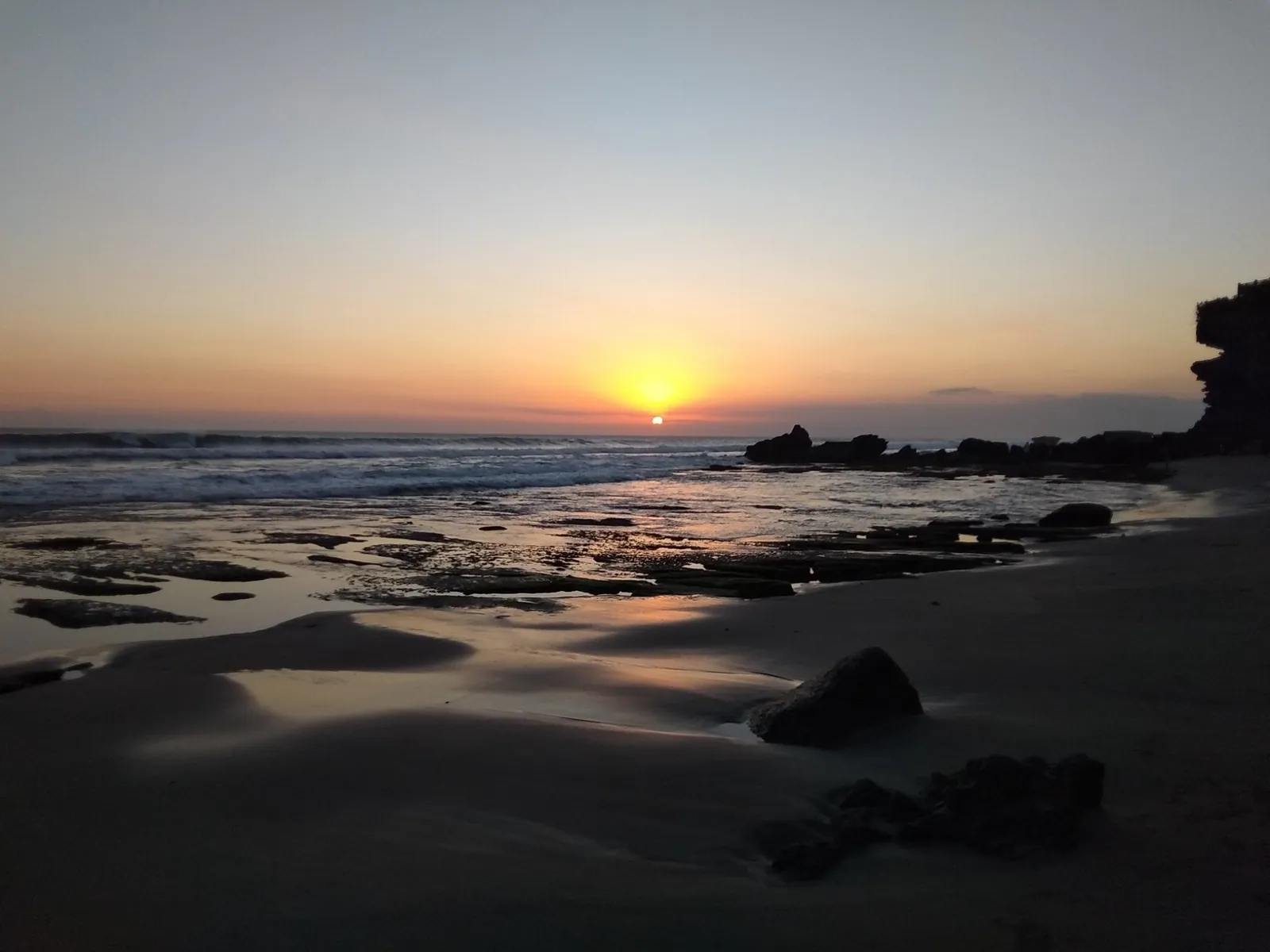 Black volcanic sand beach on Bali's south-west coast at sunset